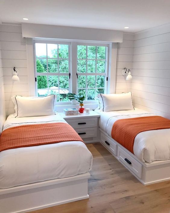 Chambre toute blanche avec deux lits et détails orange.