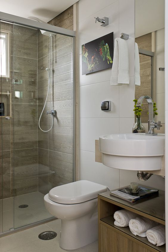 La salle de bain est décorée de tableaux, de petites plantes en pot et d'une étagère avec des serviettes apparentes.