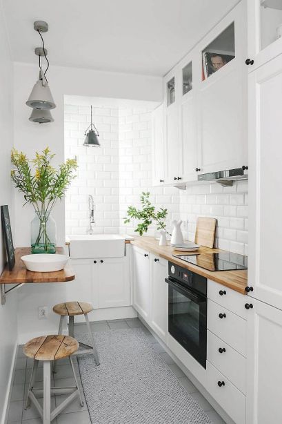 Petite cuisine d'appartement avec armoires blanches et petites étagères utilisées comme tables. 