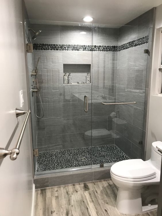 Une salle de bain moderne dans des tons gris foncé avec des inserts au sol se trouve d'un côté du mur de la douche.