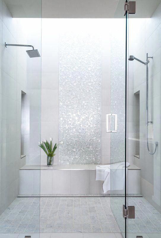 La salle de bain est conçue avec des carreaux brillants dans des tons de blanc et de gris.