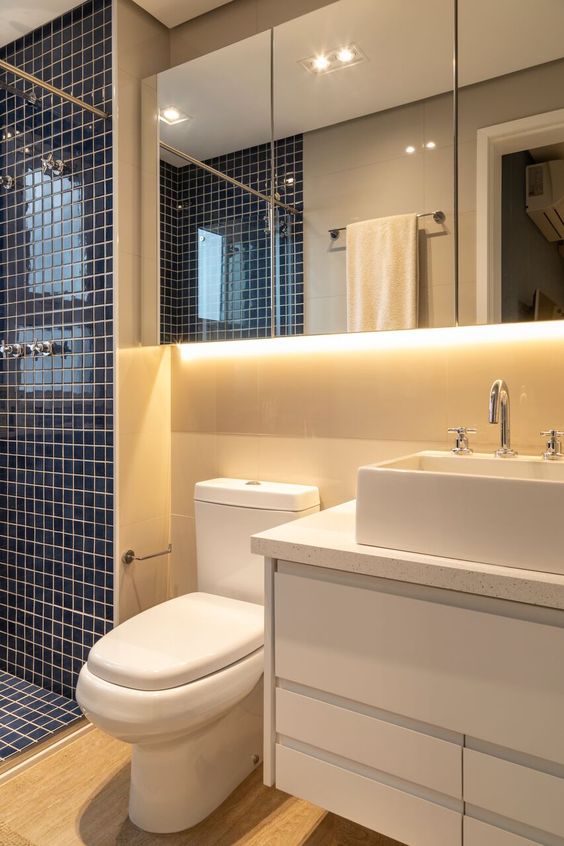 Salle de bain petit plan. Les inserts bleus et les lumières derrière les miroirs attirent l'attention et rendent l'environnement confortable.