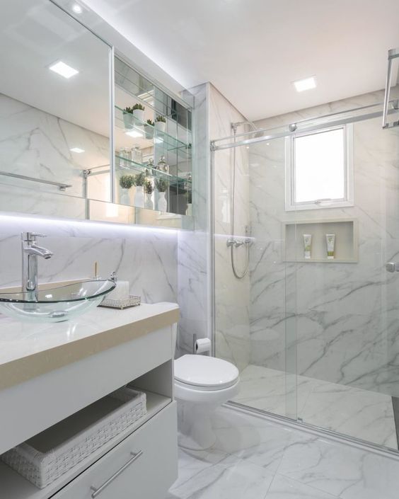 Salle de bain en marbre parfaitement propre. La lumière derrière le miroir attire l'attention. Un banc avec un bol en verre est minimaliste.