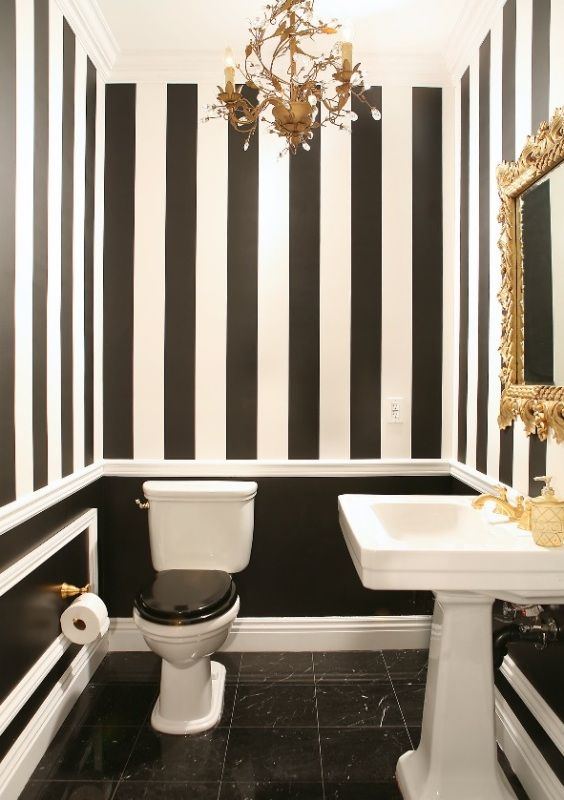 Salle de bain avec des rayures noires et blanches et des accents dorés sur les murs.