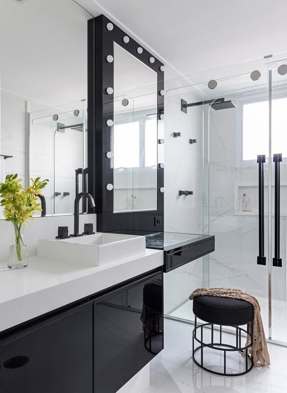 Salle de bain blanche avec armoires noires, banc et cadre de miroir.