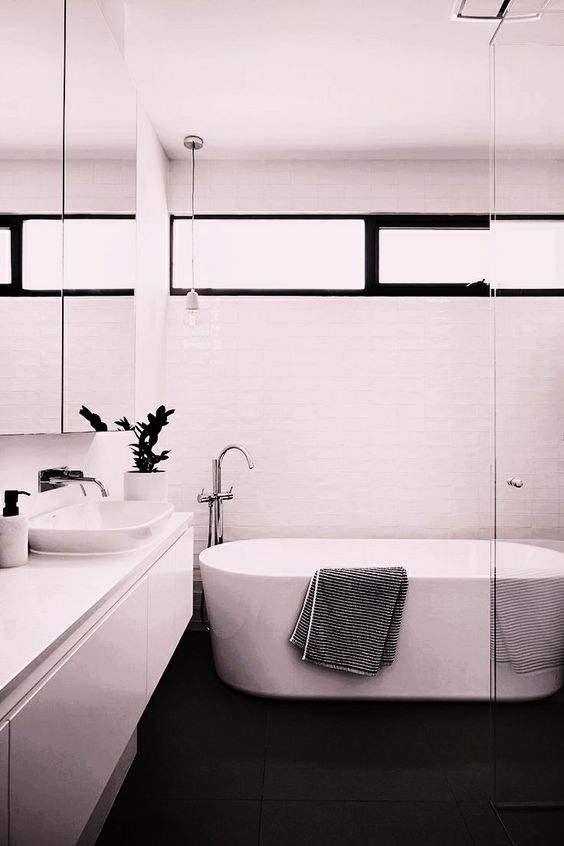 Salle de bain avec lavabo, baignoire et murs blancs et sol noir.