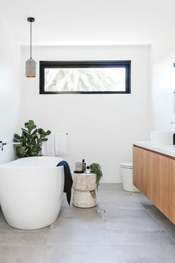 Salle de bain blanche avec des détails noirs et des plantes décoratives aux fenêtres.