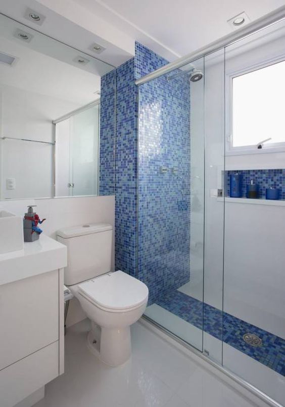 La salle de bain a un mur de douche et une alcôve encastrée avec des inserts bleus.