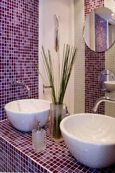 Salle de bain avec deux lavabos, des plantes en pot et des murs carrelés violets et blancs.
