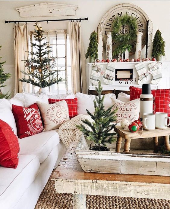 Décoration de Noël de salon simple avec petit sapin, couronne discrète et coussins rouges.